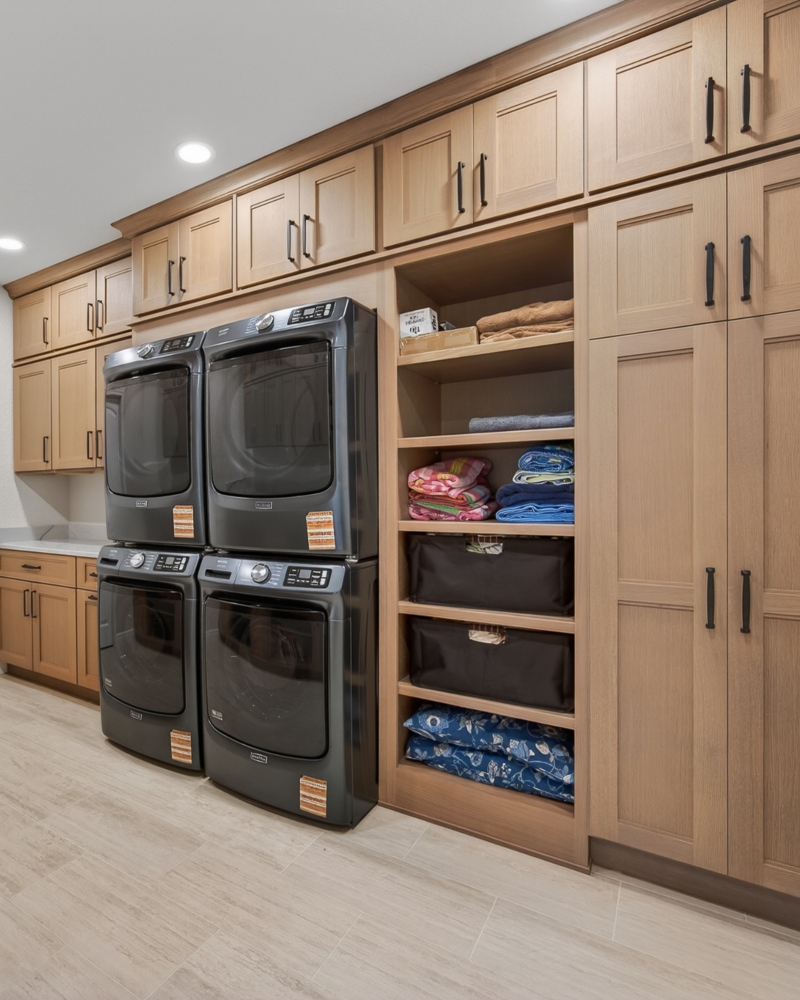 Custom laundry room with warm wood cabinetry, built-in storage and stacked washers and dryers by Ragan Cabinets.