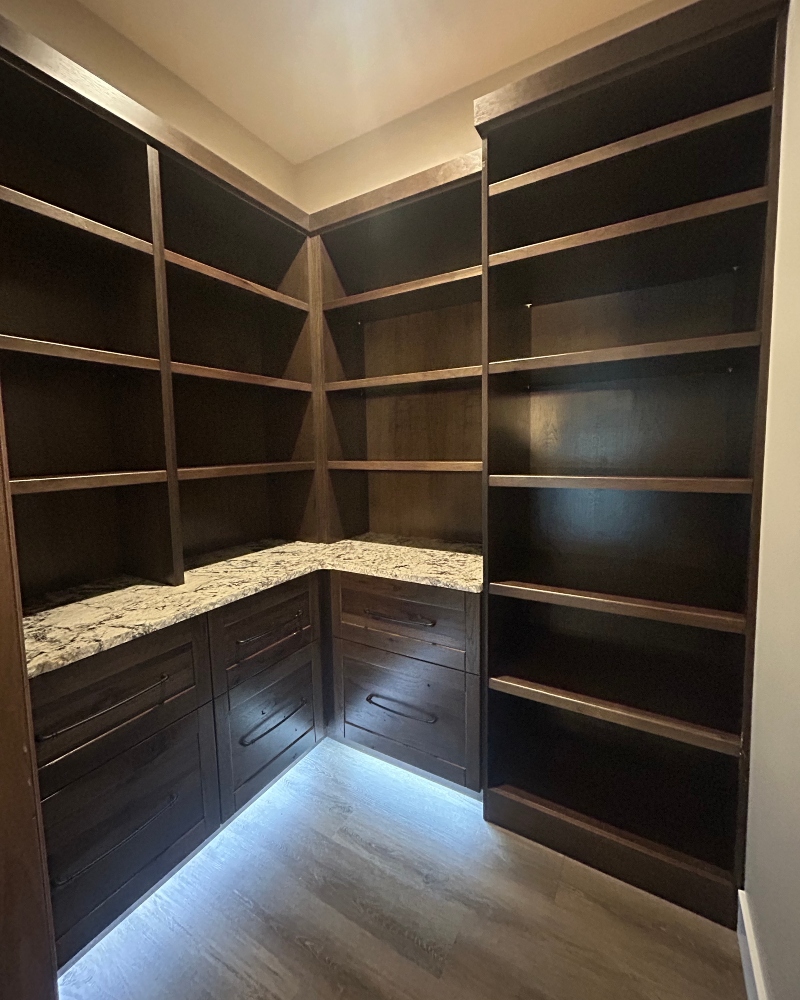 Custom walk-in pantry with dark wood cabinetry, open shelving, stone countertop and built-in storage by Ragan Cabinets.
