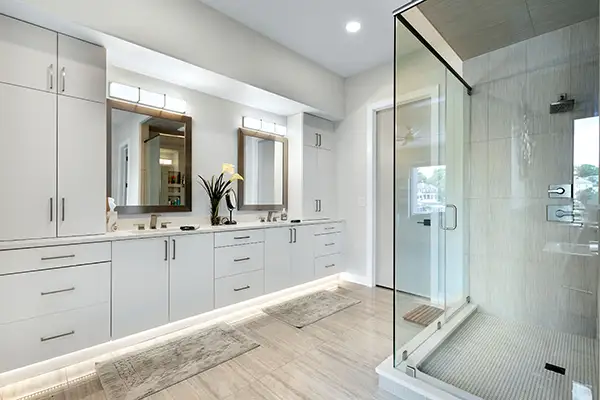 Custom bathroom with white vanity cabinetry, dual sinks, modern mirrors and glass walk-in shower by Ragan Cabinets.