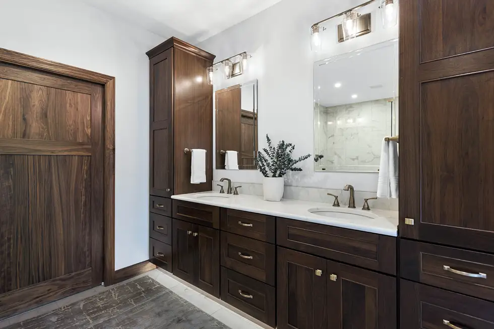 Custom Lake of the Ozarks bathroom with rich walnut double vanity, tall storage cabinetry, white countertops and brushed metal hardware by Ragan Cabinets.