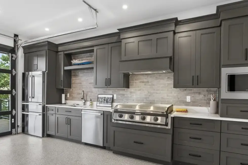 Custom Lake of the Ozarks kitchen with dark gray cabinetry, stainless appliances, built-in grill and specialty garage-style door opening to the deck.