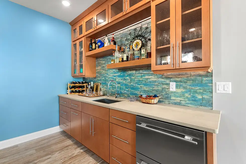 Custom Lake of the Ozarks wet bar with warm wood cabinetry, glass-front storage, floating shelves, beverage refrigeration and tile backsplash by Ragan Cabinets.