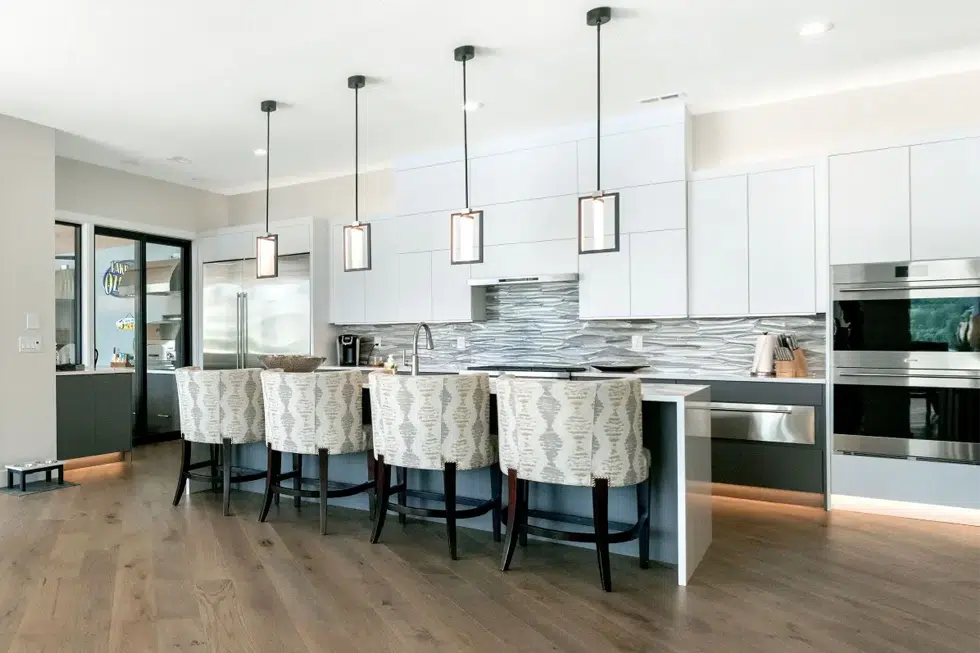 Modern Lake of the Ozarks kitchen with white cabinetry, dark lower cabinets, quartz waterfall island and contemporary pendant lighting by Ragan Cabinets.
